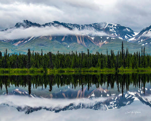 Panoramic Mountain Reflections — Snow-streaked mountains rise above a dark line of spruce, a ribbon of low cloud drifting across their flanks